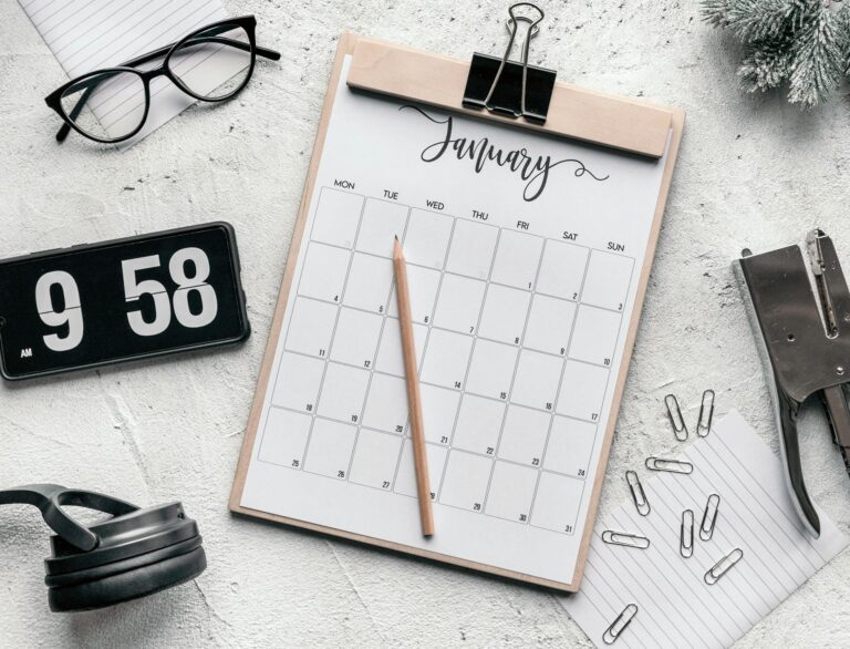 Table avec un calendrier, une horloge, des lunettes, des écouteurs et des articles scolaires.