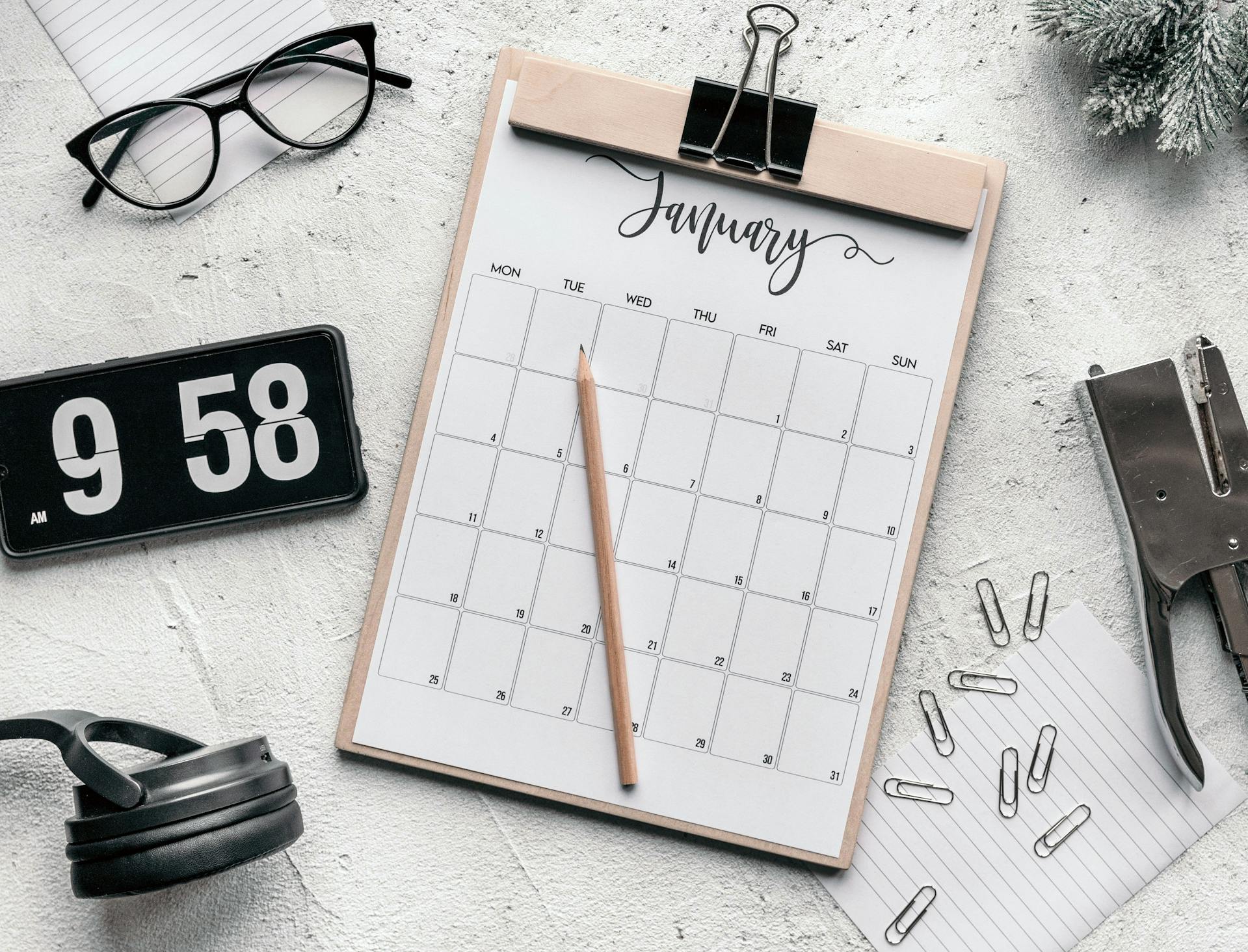 Table avec un calendrier, une horloge, des lunettes, des écouteurs et des articles scolaires.