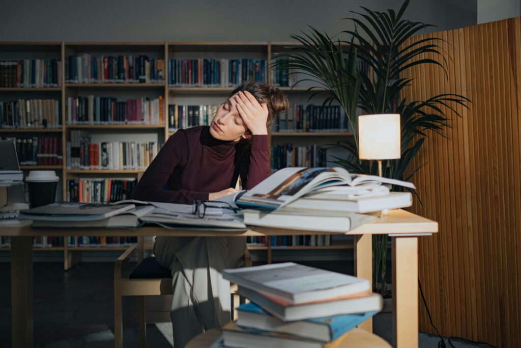 Personne découragée assise à un bureau avec pleins de cahiers.