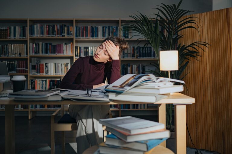 Personne découragée assise à un bureau avec pleins de cahiers.